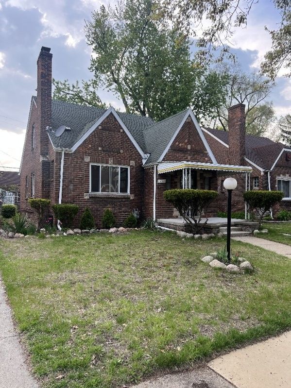 english style home featuring brick siding, a front yard, and a chimney