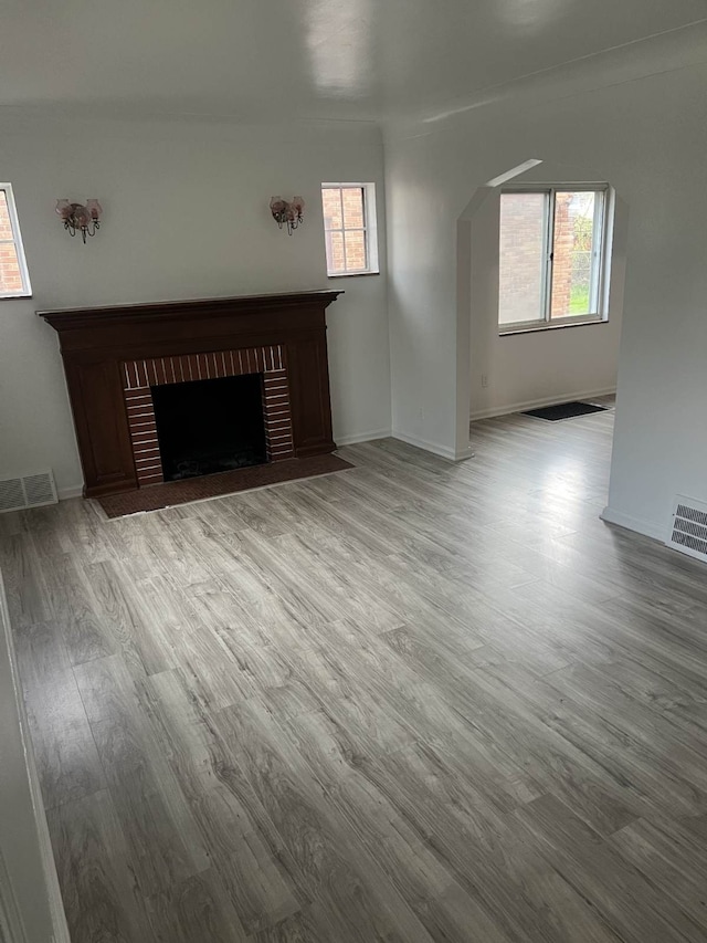 unfurnished living room featuring wood finished floors, a brick fireplace, and plenty of natural light