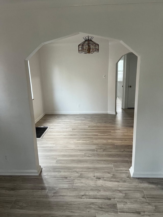 unfurnished room featuring arched walkways, wood finished floors, and baseboards