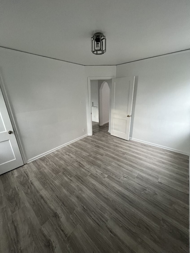 unfurnished bedroom featuring dark wood-style flooring, arched walkways, and baseboards