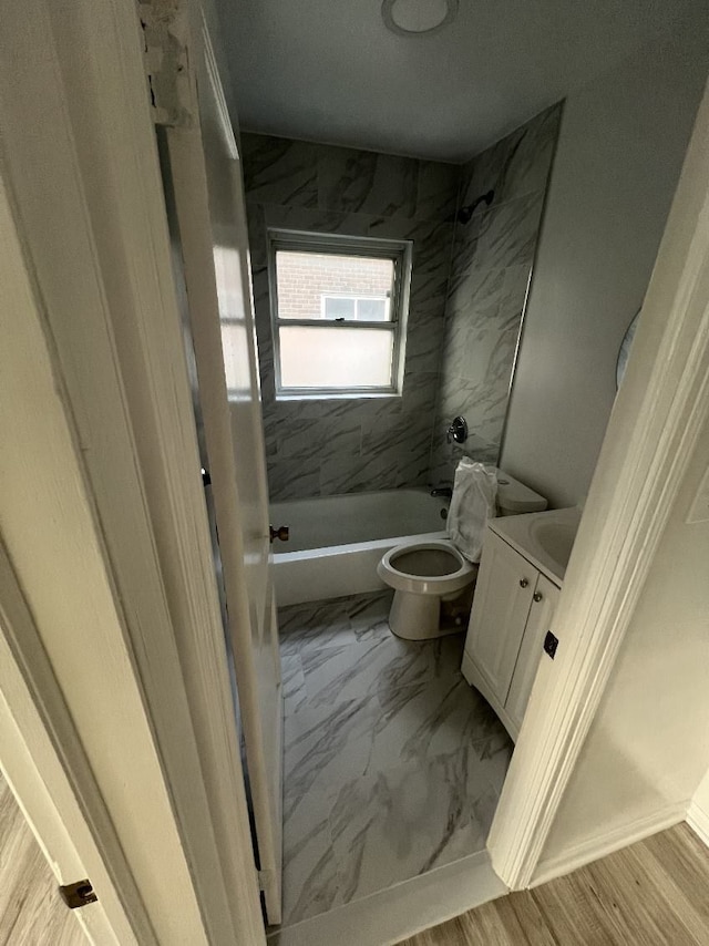 full bath with toilet, marble look tiles, vanity, and washtub / shower combination