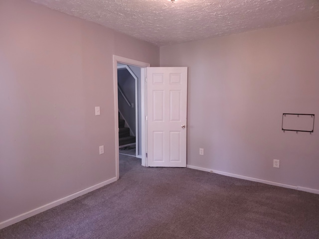 spare room with a textured ceiling, dark carpet, and baseboards