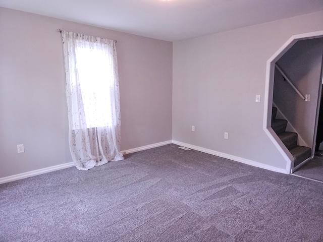 empty room featuring carpet floors, stairway, baseboards, and arched walkways
