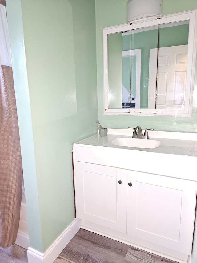 bathroom featuring wood finished floors, vanity, baseboards, and shower / tub combo