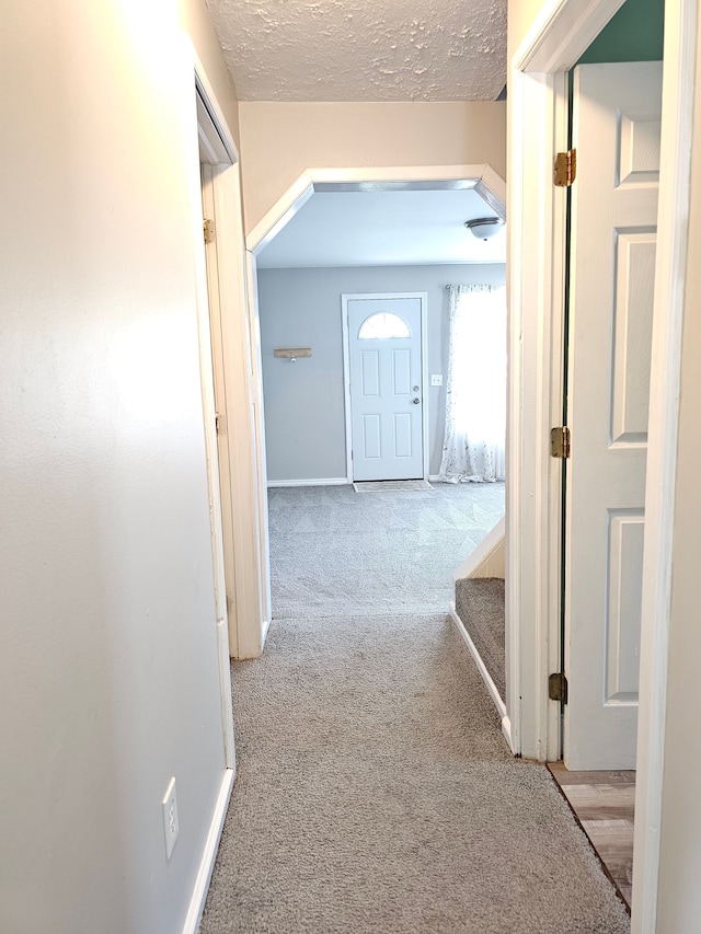 hallway featuring carpet, baseboards, and a textured ceiling