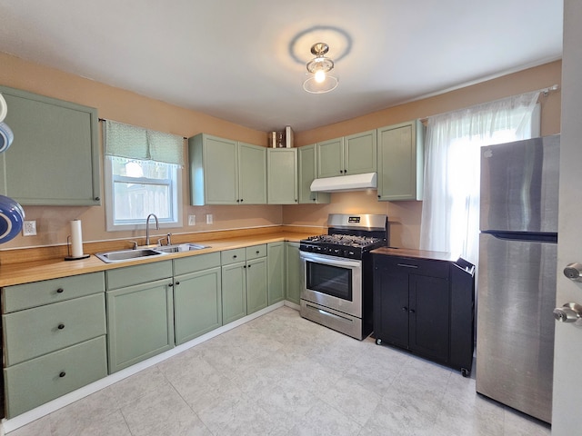 kitchen with appliances with stainless steel finishes, green cabinetry, under cabinet range hood, a sink, and light countertops