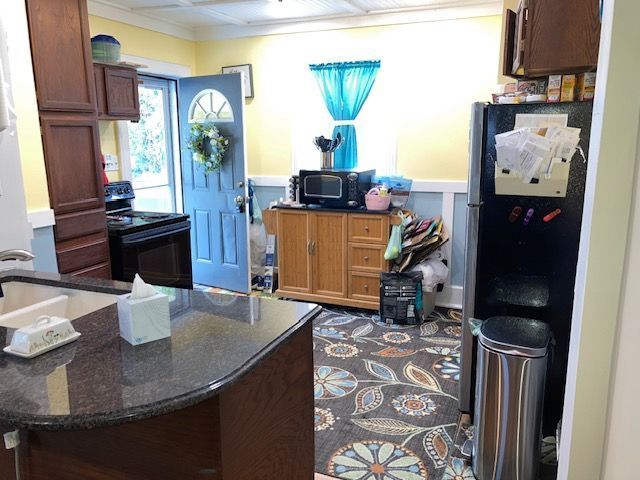 kitchen featuring black appliances, ornamental molding, dark stone counters, and a wainscoted wall