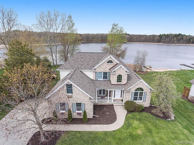 traditional-style home featuring covered porch, a water view, a front lawn, and brick siding