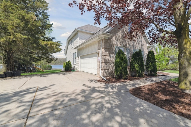 view of property exterior with driveway, an attached garage, a water view, and brick siding