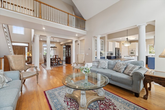 living area featuring decorative columns, light wood-style flooring, healthy amount of natural light, and high vaulted ceiling