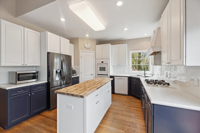 kitchen featuring appliances with stainless steel finishes, a sink, a kitchen island, white cabinetry, and recessed lighting
