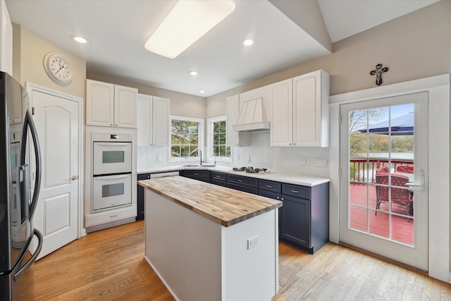 kitchen with butcher block countertops, white appliances, custom range hood, plenty of natural light, and recessed lighting