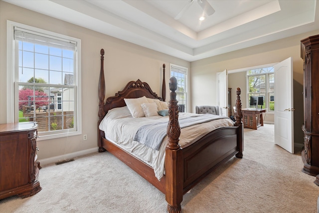 bedroom featuring light carpet, a tray ceiling, baseboards, and a ceiling fan