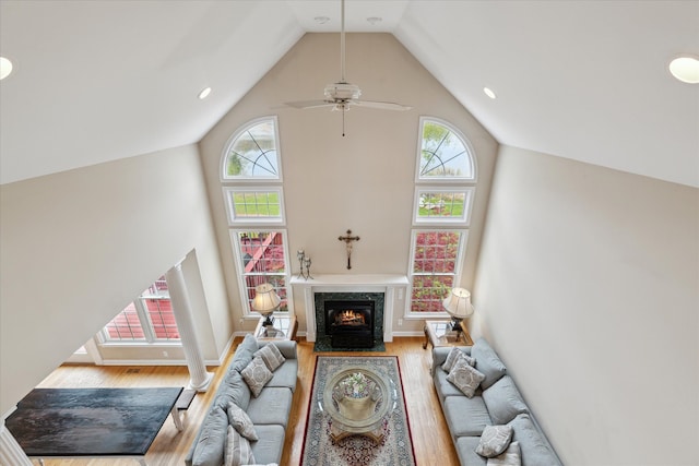 living area with high vaulted ceiling, wood finished floors, a premium fireplace, baseboards, and a ceiling fan