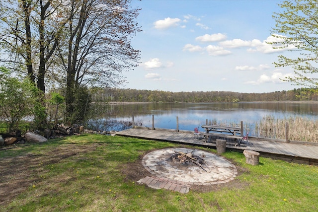 dock area featuring a fire pit, a water view, a view of trees, and a yard