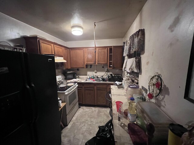 13192 Schoolcraft Rd, Detroit, MI 48227 - kitchen with freestanding refrigerator, electric range, tile countertops, under cabinet range hood, and brown cabinetry