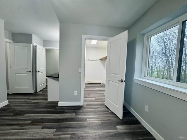 3339 S Cabaret Trl, Saginaw, MI 48603 - unfurnished bedroom with baseboards, dark wood-style flooring, baseboard heating, and a spacious closet