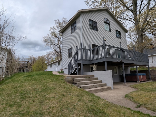 back of house featuring a hot tub, a deck, a lawn, and stairway