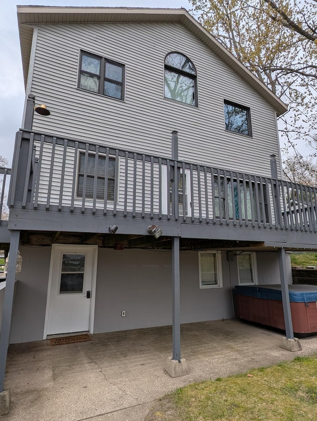 rear view of property with a hot tub, a patio, and a wooden deck