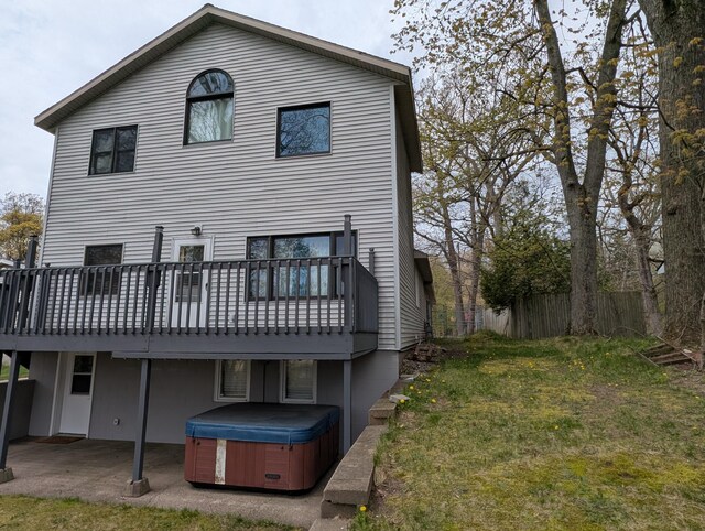 rear view of property featuring a hot tub, a patio, a deck, and a lawn