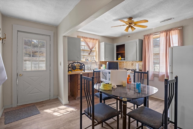 dining room featuring a textured ceiling, light wood-style flooring, ceiling fan, and baseboards