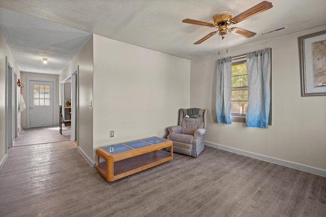 living area with baseboards, wood finished floors, and a ceiling fan