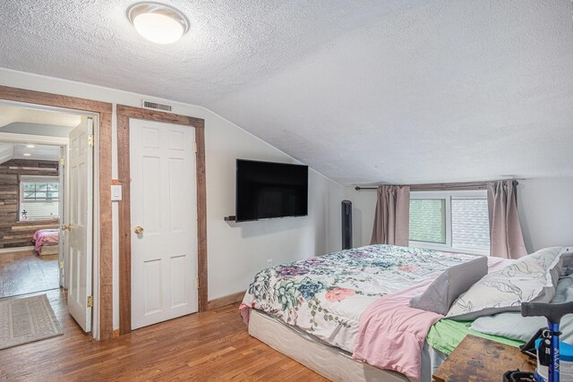 bedroom with a textured ceiling, wood finished floors, lofted ceiling, and baseboards