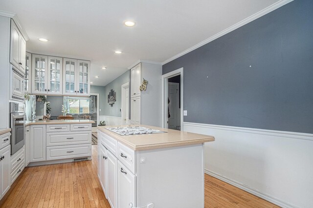 kitchen featuring appliances with stainless steel finishes, glass insert cabinets, light wood-style flooring, light countertops, and white cabinetry