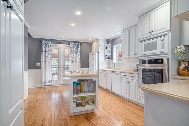 kitchen featuring open shelves, stainless steel appliances, ornamental molding, wainscoting, and light wood finished floors