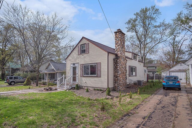 bungalow-style home with cooling unit, a front yard, a chimney, and an outdoor structure