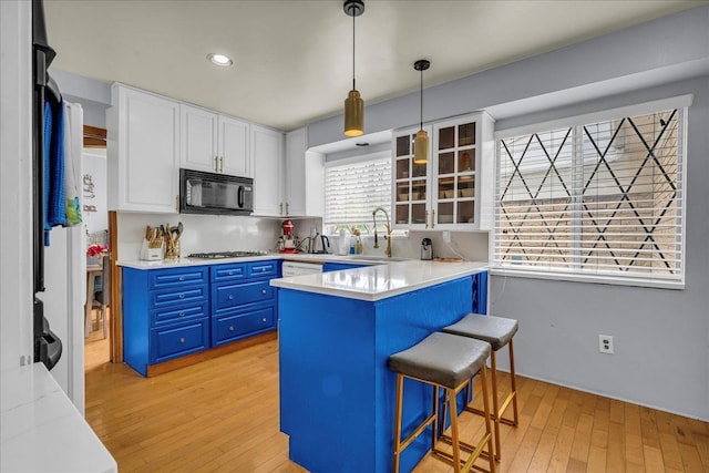 18579 Jeanette St, Southfield, MI 48075 - kitchen with black microwave, blue cabinetry, a kitchen bar, white cabinetry, and light wood-type flooring