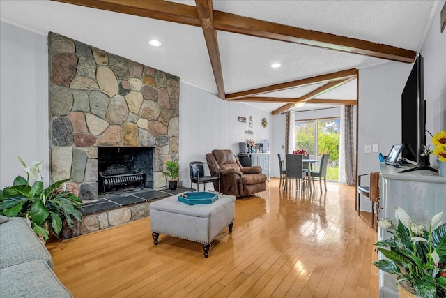 18579 Jeanette St, Southfield, MI 48075 - living room with beamed ceiling, hardwood / wood-style floors, wood walls, a stone fireplace, and a textured ceiling