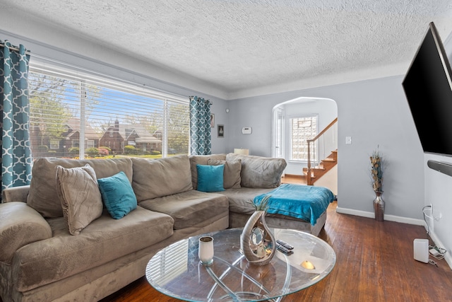 living room with wood-type flooring, healthy amount of natural light, arched walkways, stairs, and a textured ceiling