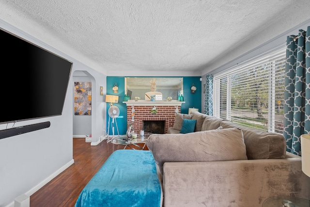 living area with a textured ceiling, baseboards, wood finished floors, a brick fireplace, and arched walkways