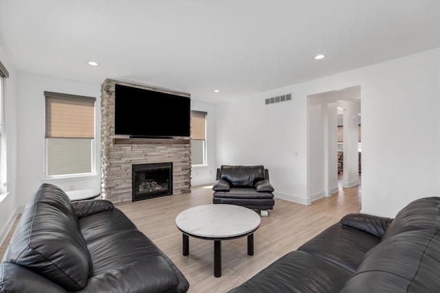 living room featuring light wood-type flooring, baseboards, recessed lighting, and a stone fireplace