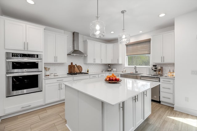 kitchen featuring wall chimney range hood, a sink, stainless steel appliances, light countertops, and white cabinetry