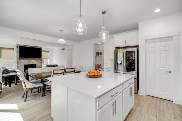kitchen featuring stainless steel fridge with ice dispenser, a kitchen island, white cabinetry, a fireplace, and light countertops