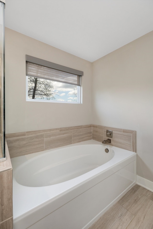 bathroom with a garden tub, wood finished floors, and baseboards