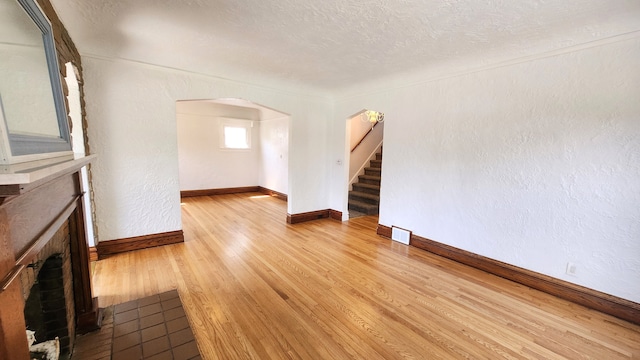 unfurnished living room with a fireplace, light wood finished floors, arched walkways, stairs, and baseboards