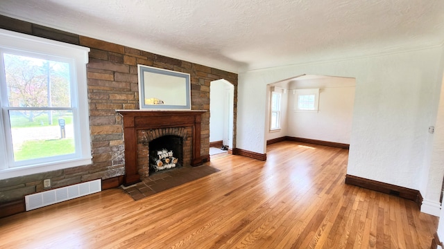 unfurnished living room with a textured ceiling, light wood-type flooring, a fireplace, baseboards, and arched walkways