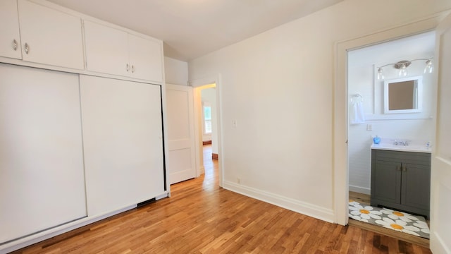 unfurnished bedroom with light wood-type flooring, a sink, a closet, ensuite bath, and baseboards