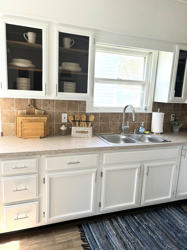 kitchen with a sink, white cabinetry, backsplash, and glass insert cabinets