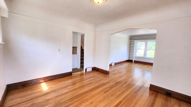 unfurnished room with light wood-type flooring, baseboards, arched walkways, and a textured wall