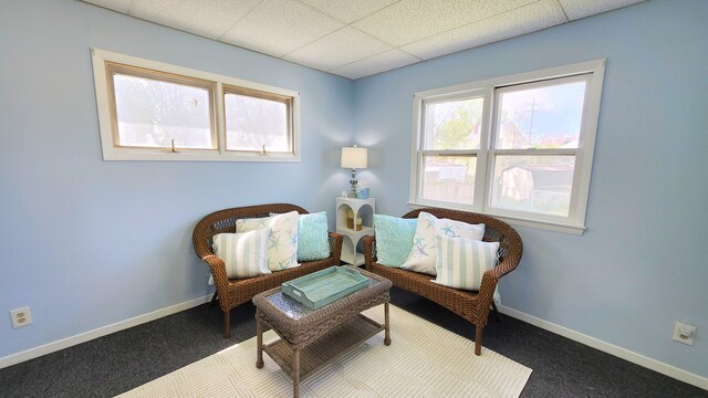 living area with a drop ceiling, carpet, and baseboards