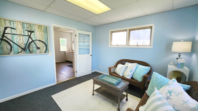 living area featuring a drop ceiling, carpet flooring, and baseboards