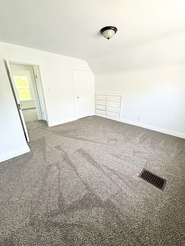 empty room featuring carpet, baseboards, and vaulted ceiling