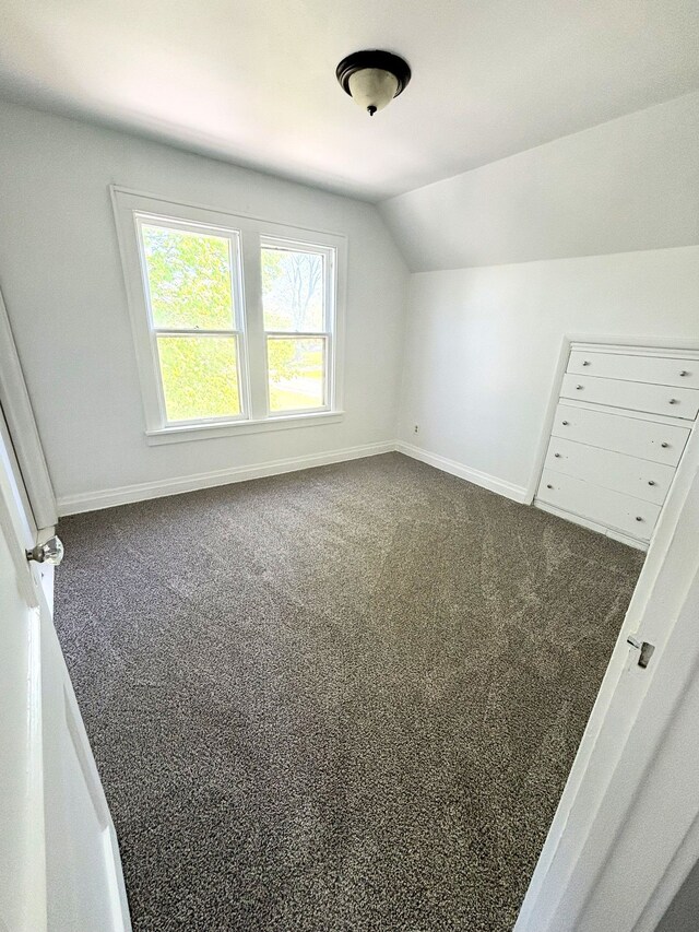 bonus room featuring lofted ceiling, dark carpet, and baseboards