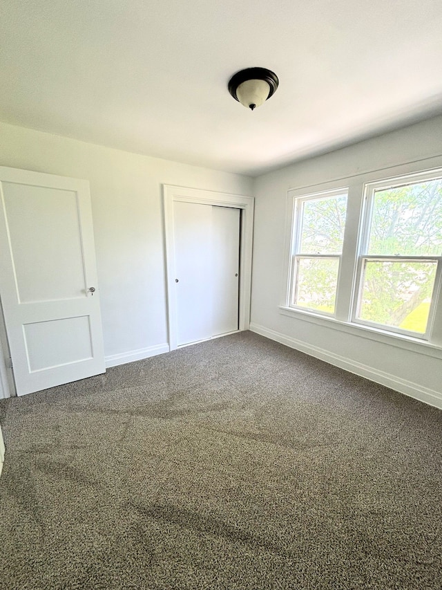 unfurnished bedroom featuring baseboards, dark carpet, and a closet
