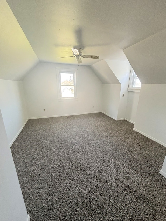 additional living space with vaulted ceiling, plenty of natural light, a ceiling fan, and dark carpet