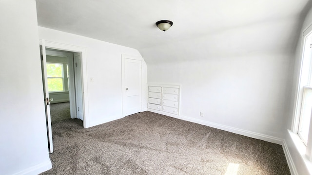 additional living space featuring dark carpet, vaulted ceiling, and baseboards